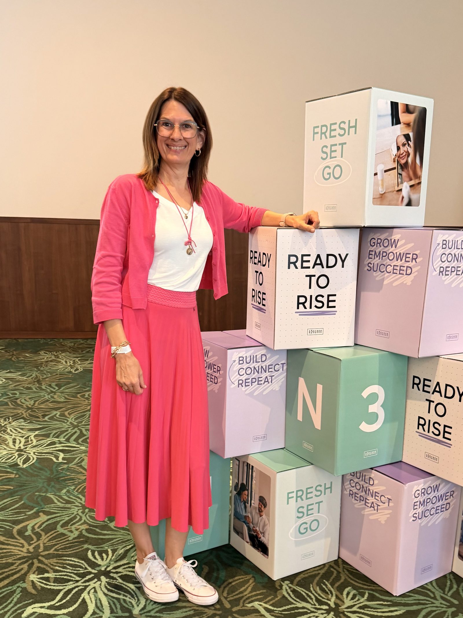 Bettina Höld in Pink vor gestapelten Boxen mit der Aufschrift „Ready to Rise“